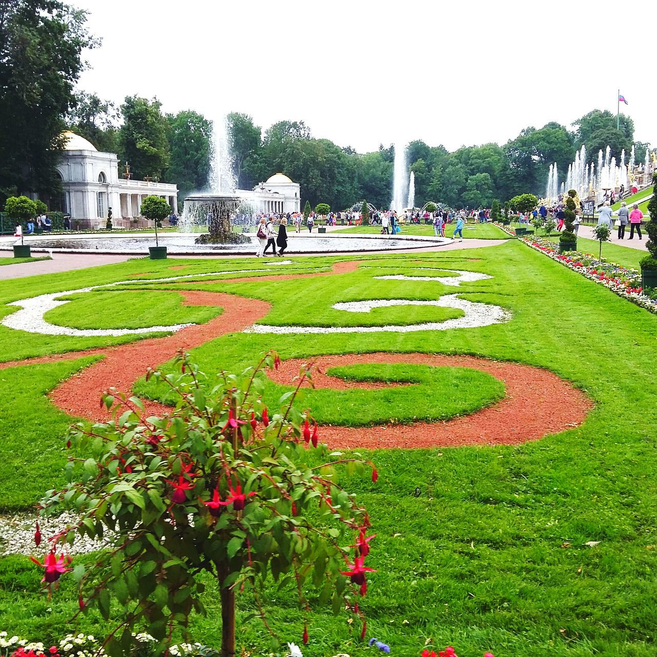 flower, grass, freshness, green color, park - man made space, growth, tree, incidental people, city, formal garden, fragility, plant, beauty in nature, tranquility, day, nature, footpath, spraying, fountain, tranquil scene, water, outdoors, city life, park, ornamental garden, decoration, scenics, garden path