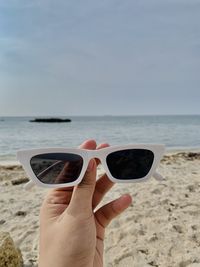 Cropped hand of woman wearing sunglasses on beach