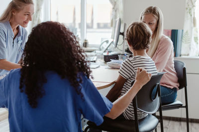 Mother and son consulting doctor while female nurse sitting by desk in clinic