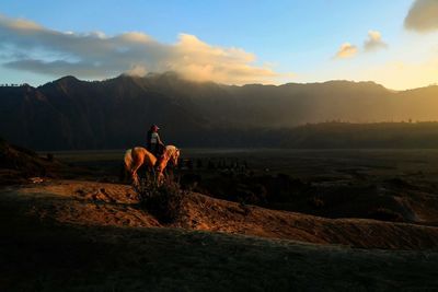 Person horseback riding on mountain against sky during sunset