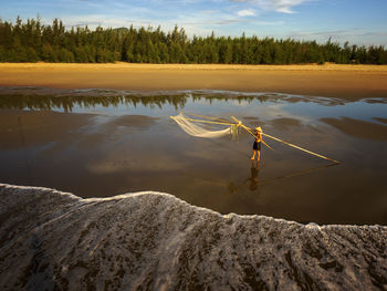 Fisherman with fishing nets standing at beach against sky during sunset