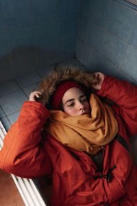 From above of young lady in bright outerwear napping with closed eyes in bathtub in house