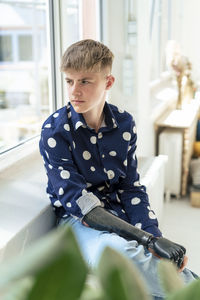 Thoughtful teenage boy with amputated arm looking out through window