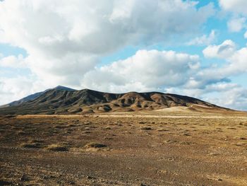 Scenic view of arid landscape against cloudy sky