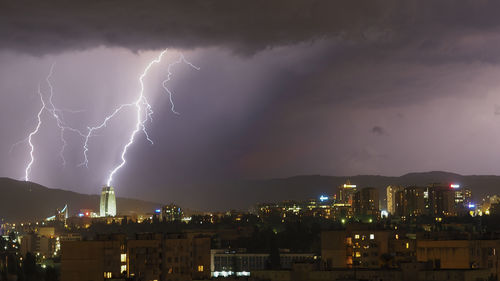 Lightning over illuminated cityscape against dramatic sky