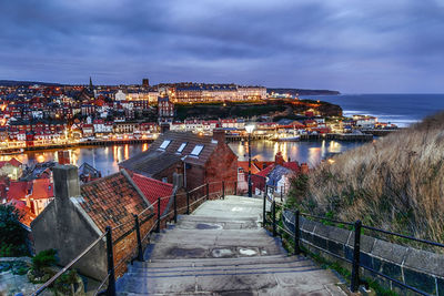 High angle view of illuminated city by sea against sky