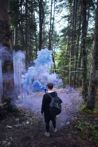 Rear view of man holding distress flare while standing in forest