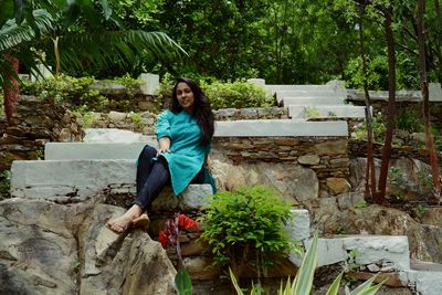 Portrait of smiling young woman sitting on steps in forest