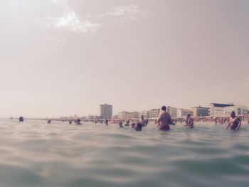 People on sea by city against sky