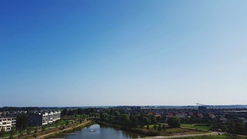 High angle view of river amidst buildings against clear blue sky