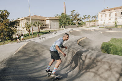 Man skateboarding on sports ramp with friends at park