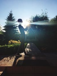 Boy standing by tree against sky