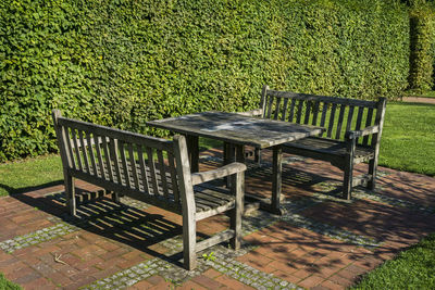 Empty wooden table and benches arranged by plants at britzer garten