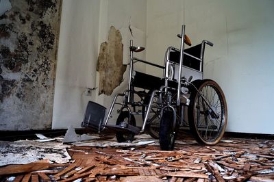 Abandoned wheelchair against broken wall at home