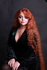 Portrait of beautiful woman with redhead sitting against black background