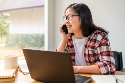 Young woman using mobile phone while sitting on table