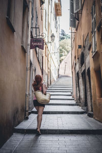 Rear view of woman walking on footpath amidst buildings