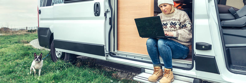 Woman teleworking sitting in the door of a camper van