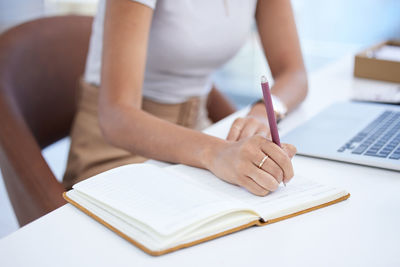 Midsection of woman writing in book at office