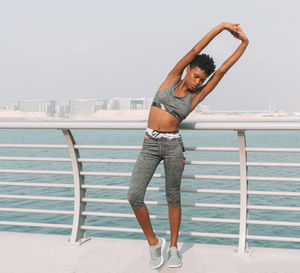 Woman stretching hands while standing on pier over sea