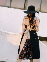 Woman holding hat standing against built structure