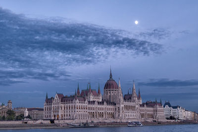 View of city at waterfront against cloudy sky