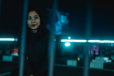 Close-up portrait of young woman standing against illuminated lights