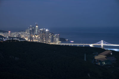 Illuminated city by sea against sky at night