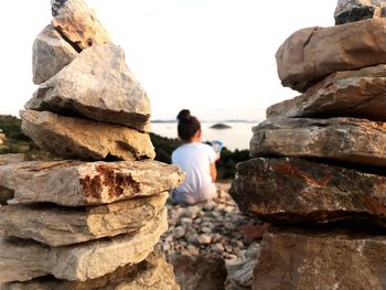 Rear view of girl sitting at beach by rock stack