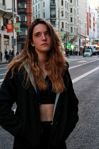 Beautiful young woman looking away while standing on street in city