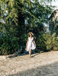 Young woman in white summer dress walking on path in city. park, greenery, lifestyle, one person.