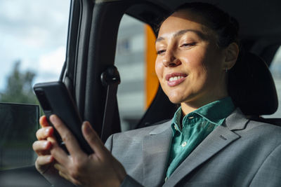 Smiling businesswoman surfing net through mobile phone in car