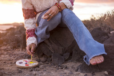 High angle view of painter with palette and brush while sitting on rock at beach