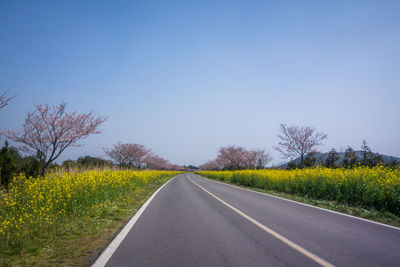 Road passing through landscape against clear blue sky