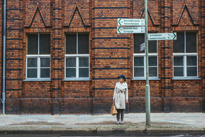 Woman waiting at bus stop while standing on sidewalk