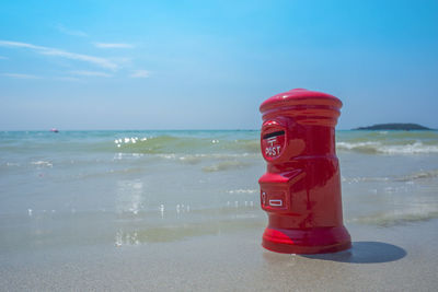 Red container on beach against sky