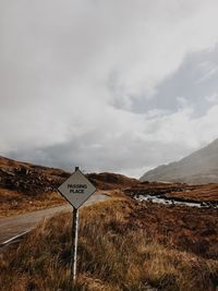 Road sign on field against sky