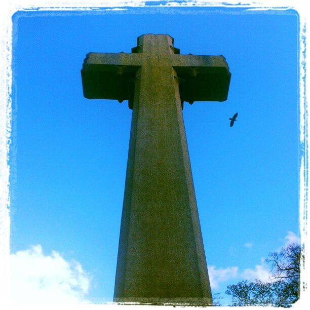 low angle view, blue, sky, religion, tree, cross, built structure, tower, tall - high, clear sky, auto post production filter, architecture, no people, day, outdoors, transfer print, street light, spirituality, pole