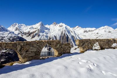 Broken arch bridge by snowcapped mountains against blue sky