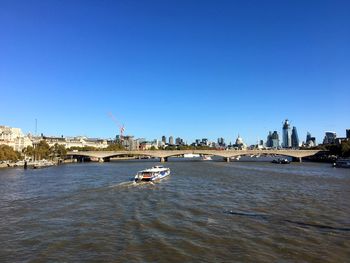 Boat in river by buildings against clear blue sky