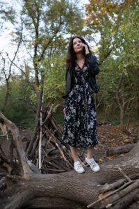 Full length of woman standing on fallen tree at forest