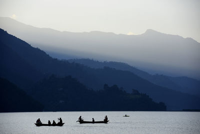 Silhouette people on lake by mountains against sky