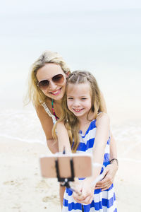 Smiling girl taking selfie with mother at beach