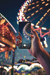 Close-up of hand holding illuminated carousel at amusement park