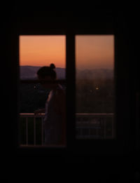 Side view of young faceless lady standing in a balcony with magnificent sunset on blurred background