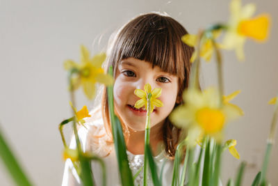 Smiling little girl behind bright yellow daffodil flowers