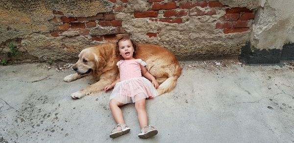 High angle portrait of baby girl lying on dog against brick wall