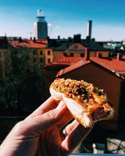 Cropped hand holding hot dog against buildings