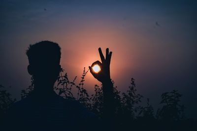 Optical illusion of silhouette mature man holding sun against sky during sunset