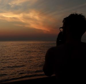 Silhouette man by sea against sky during sunset